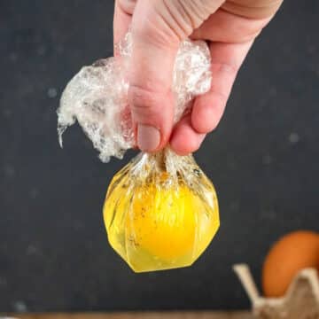 Raw egg in plastic bag held by hand.