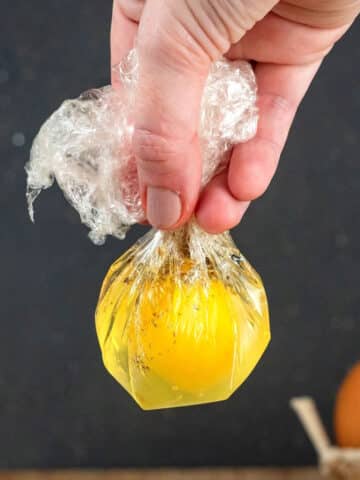 Raw egg in plastic bag held by hand.