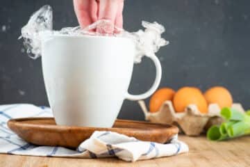 Hand pushing plastic wrap in mug.