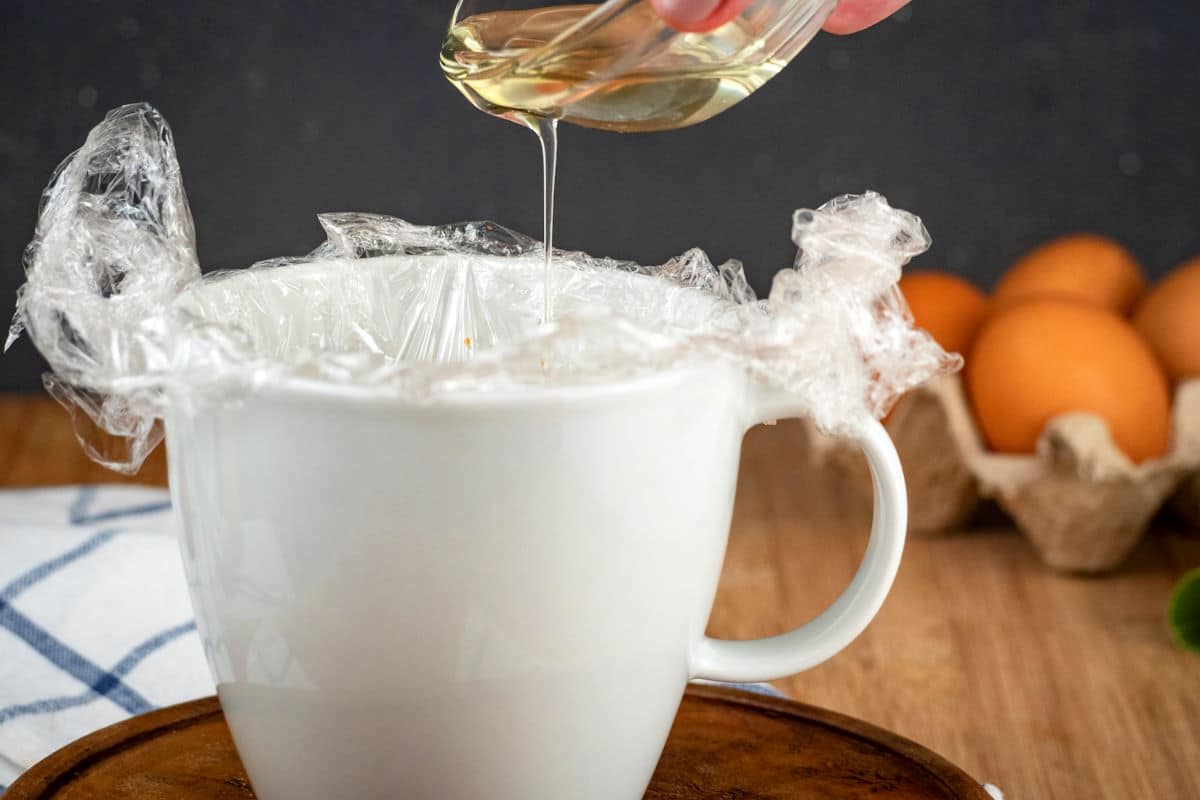 Canola oil pouring into plastic-wrap lined mug.