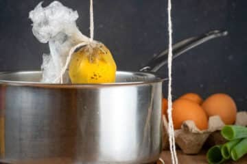 Raw egg in plastic wrap held over pot with twine.
