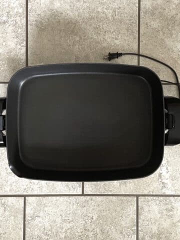 Black electric skillet on tile background.
