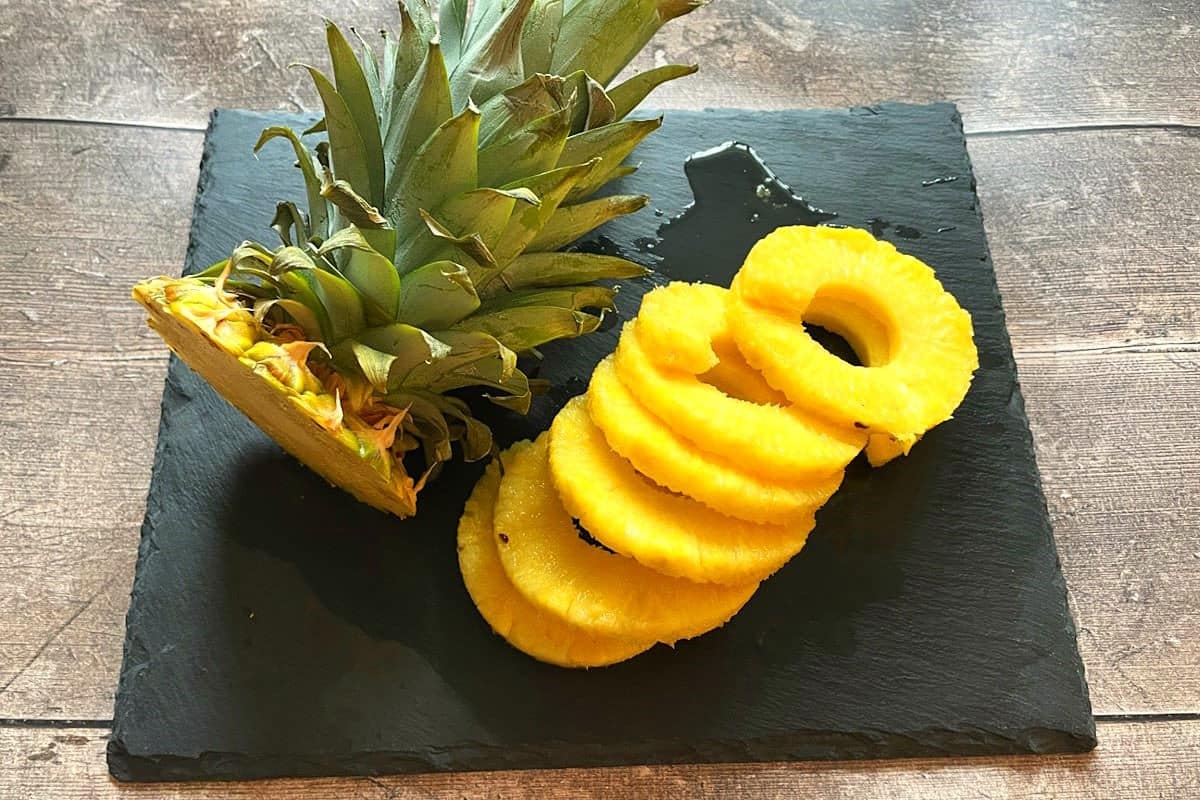 Cored and skinned, pineapple rings on black board.