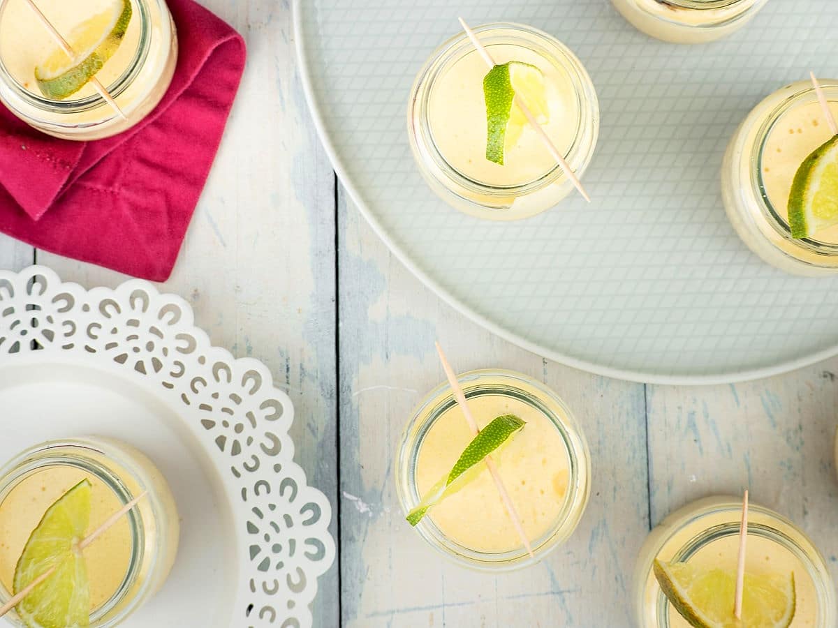 Iced lemon mousse in small jars on white wooden background.