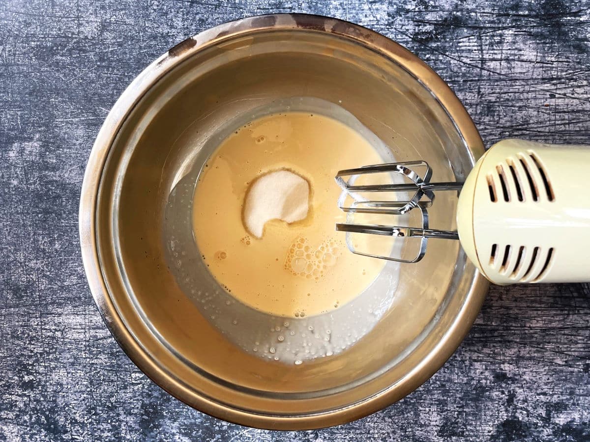Evaporated milk and sugar in bowl with electric hand mixer.