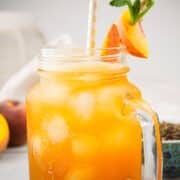 Iced peach green tea in glass with straw and peach garnish.