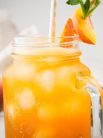 Iced peach green tea in glass with straw and peach garnish.