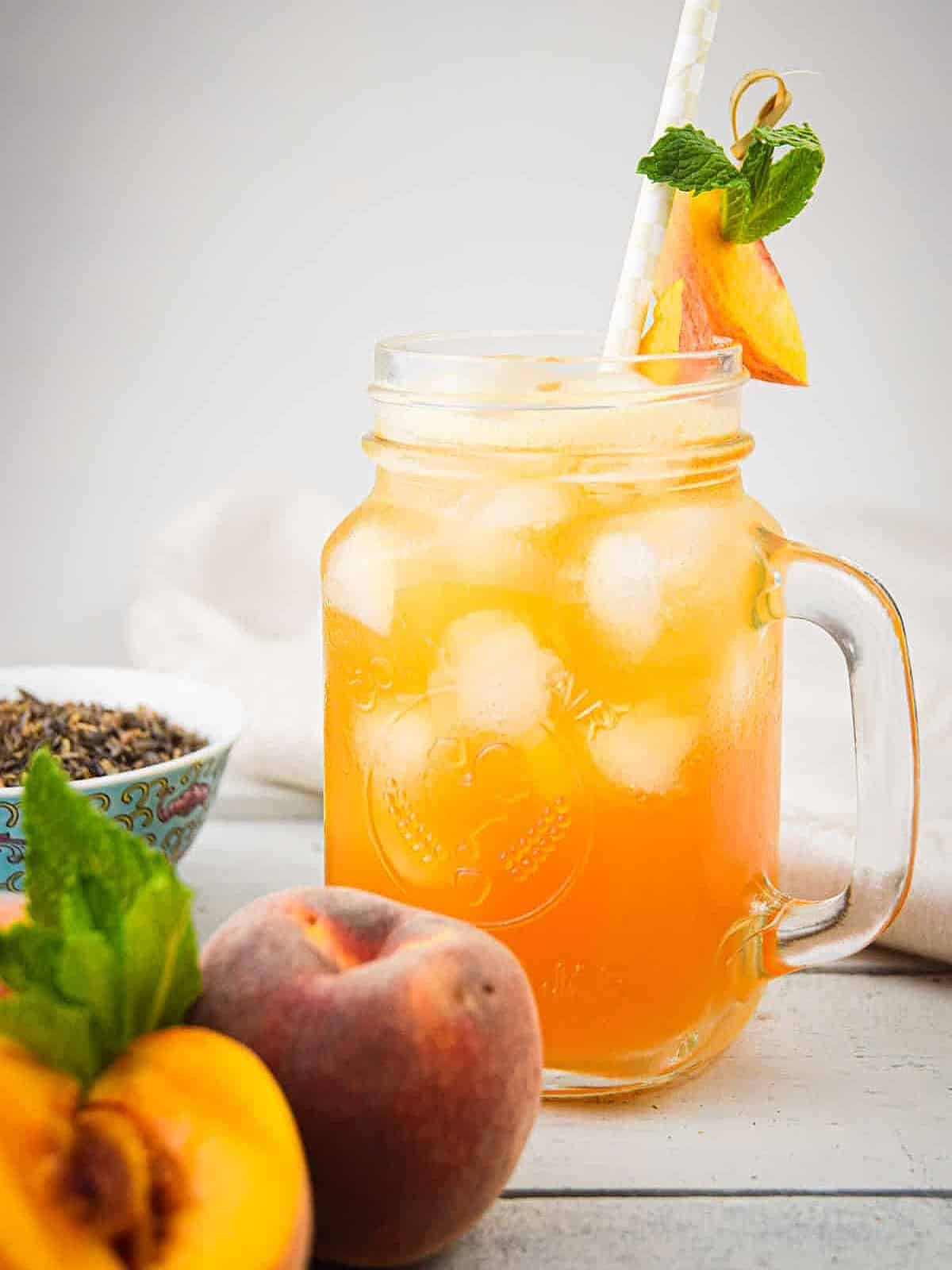 Iced peach green tea in glass with fresh peaches on the side.