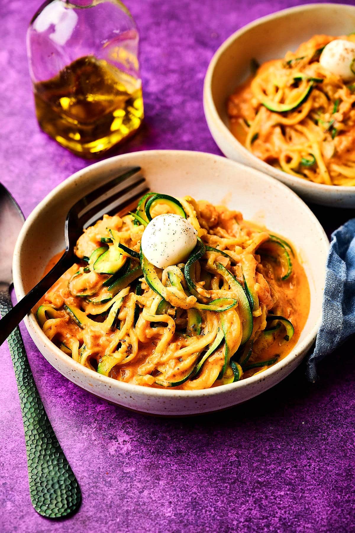 Zucchini noodles in bowls with bocconcini cheese balls on purple background.