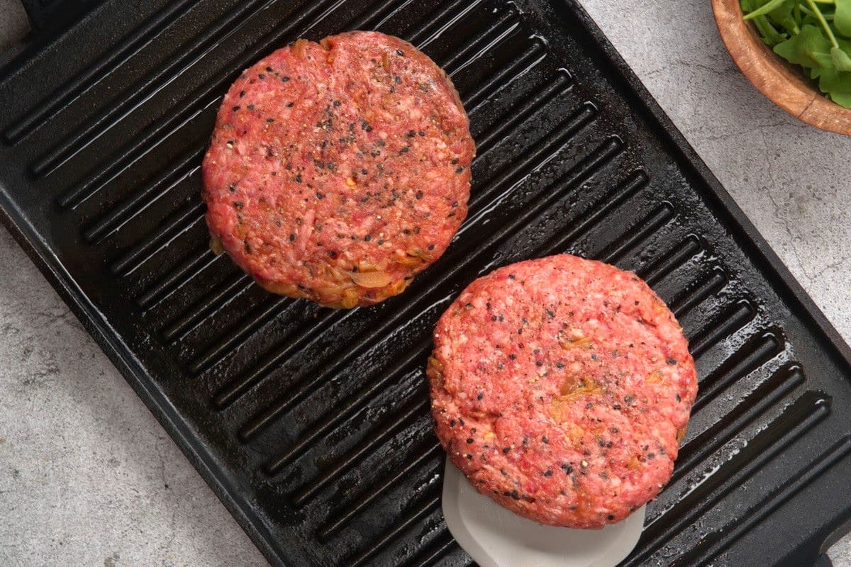 Grill pan with raw hamburger patties.