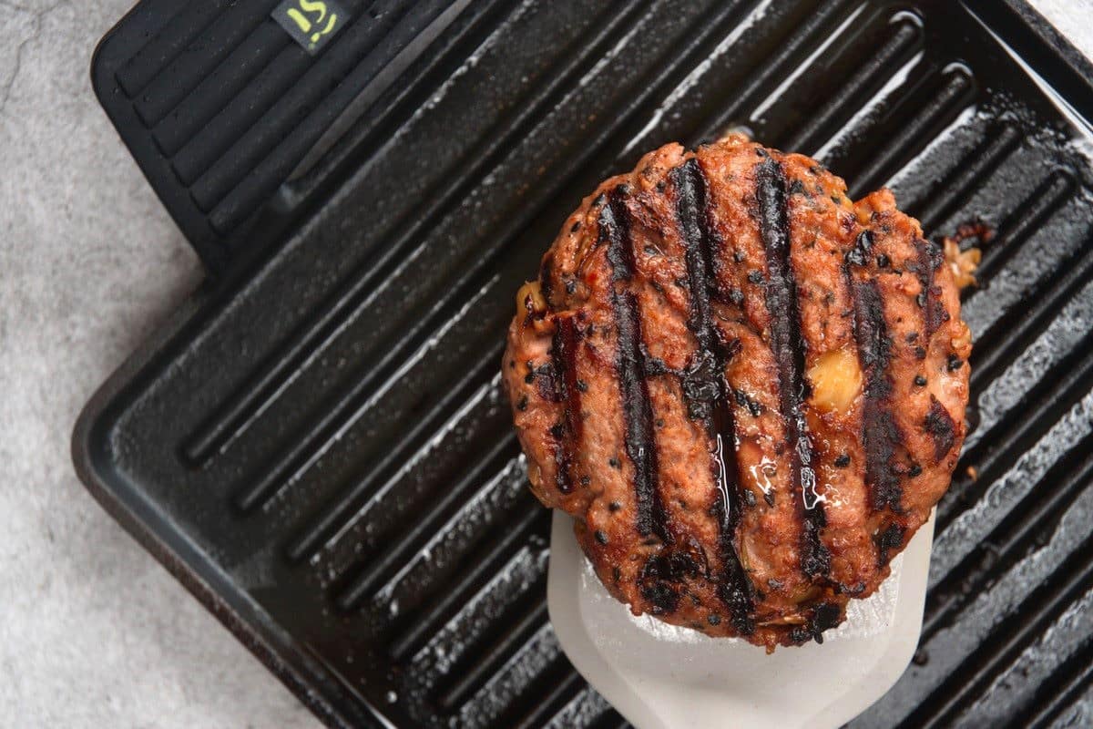 Cooked hamburger patty on spatula over grill pan.