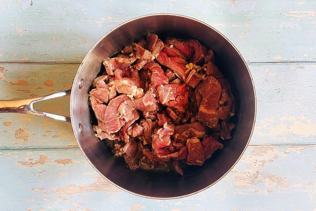 Beef sirloin strips in pot with garlic.