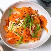 Kimchi and crab slaw in bowl with green onions and black sesame seeds.