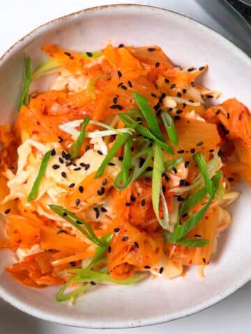 Kimchi and crab slaw in bowl with green onions and black sesame seeds.