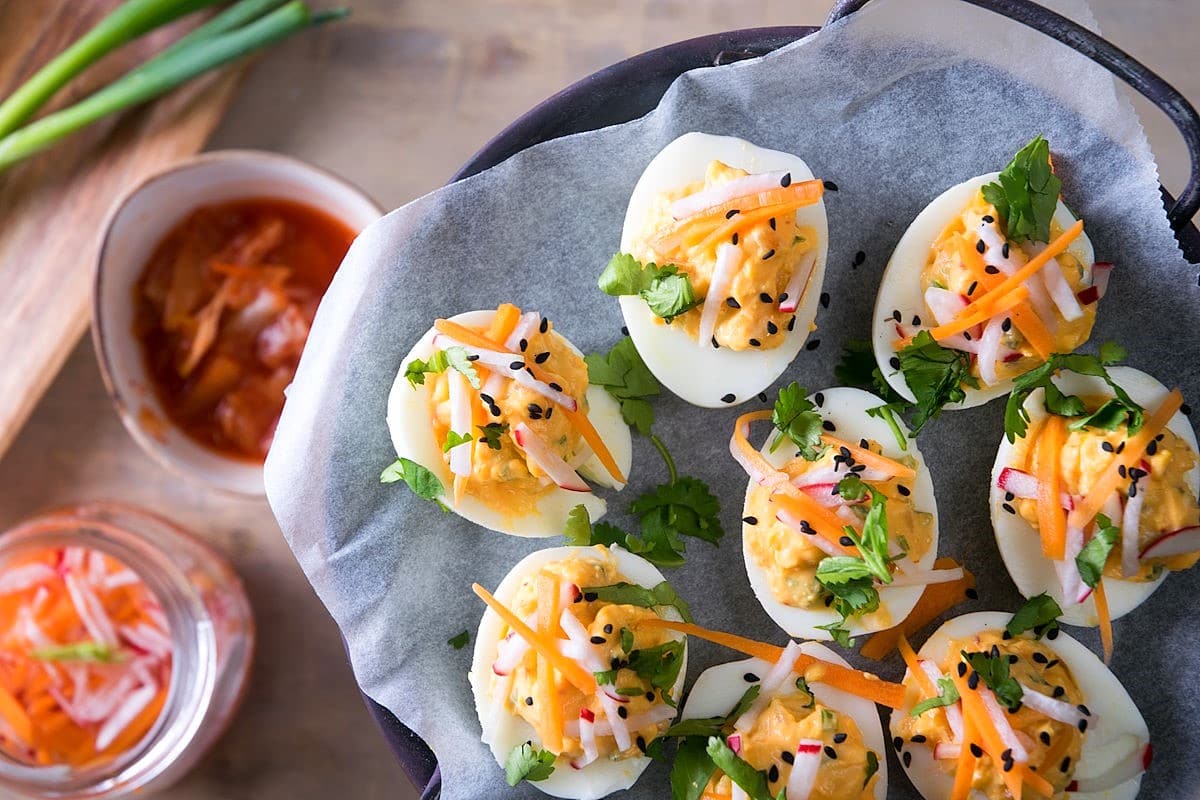 Deviled eggs with kimchi, pickled veggies and cilantro on parchment.