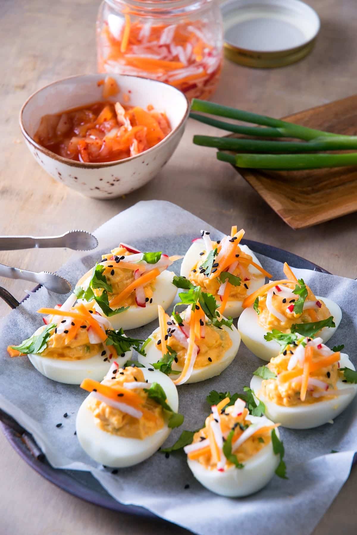 Kimchi deviled eggs on a plate with kimchi in a small bowl in the background.