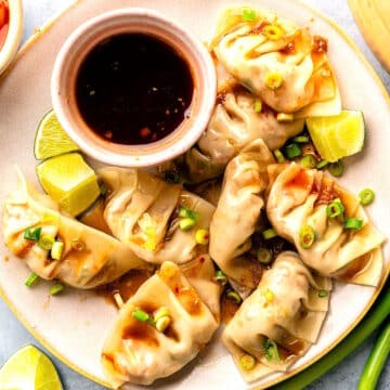 Kimchi dumplings arranged on plate with dipping sauce.
