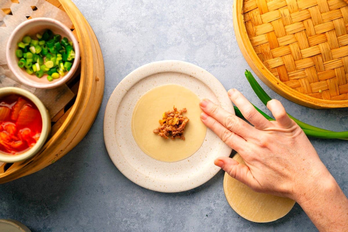 Dumpling wrapper with kimchi filling and woman's hand dabbing the wrapped with water.