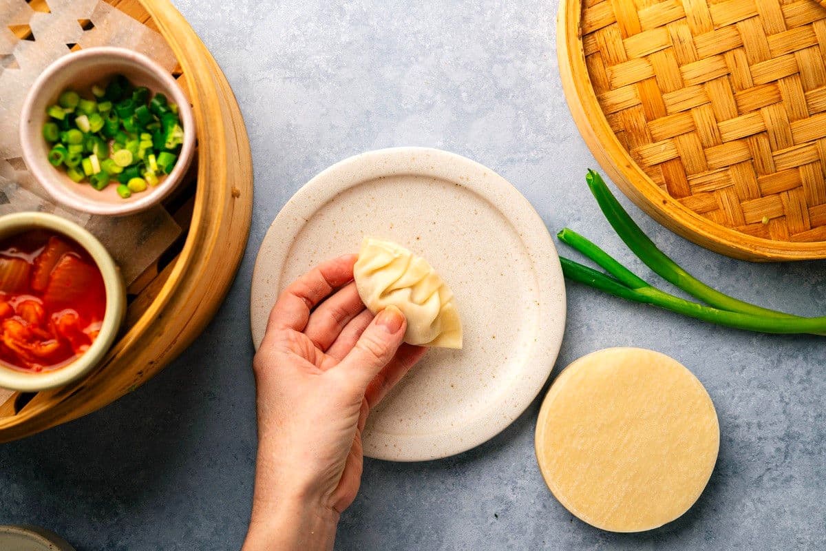 Folded, raw kimchi dumpling in woman's hand.