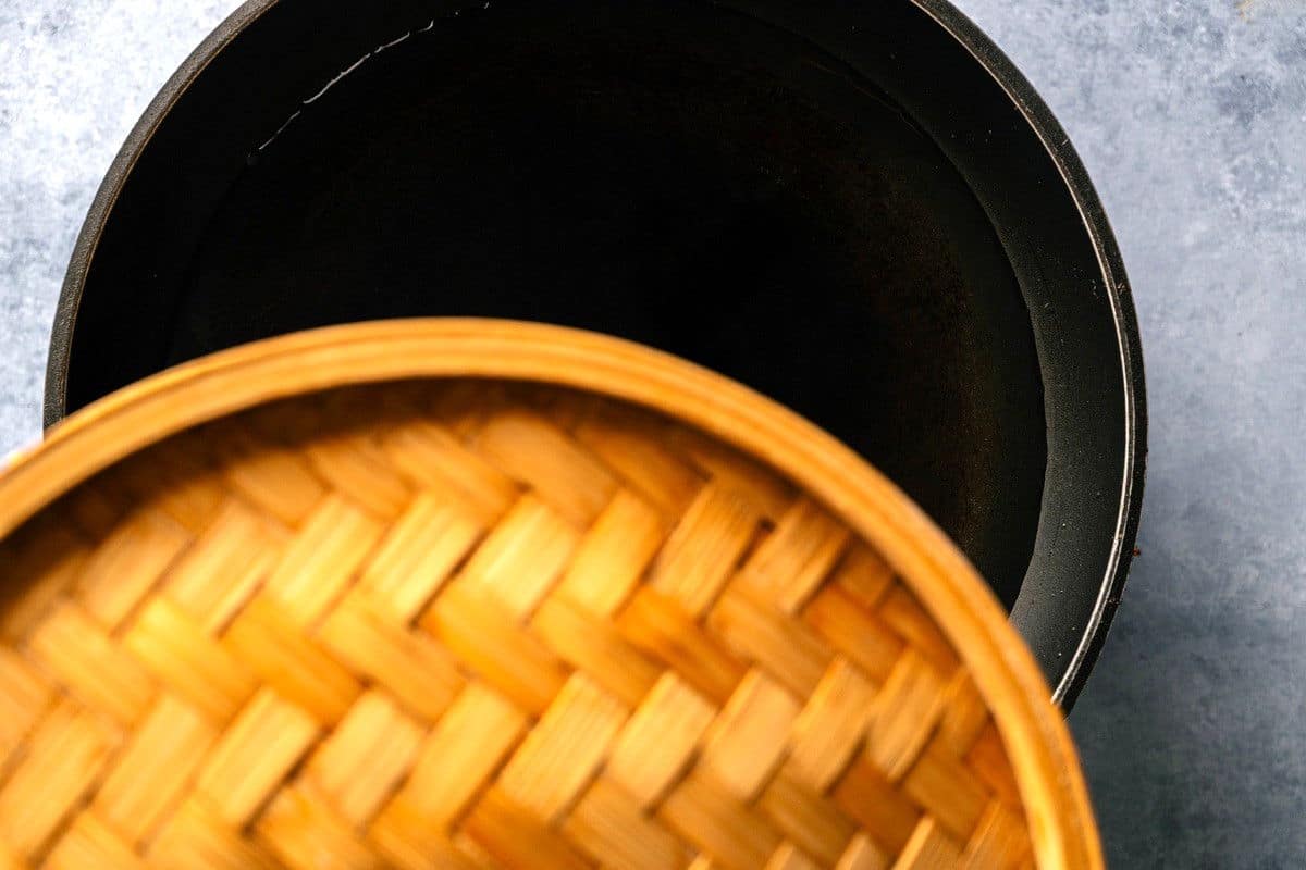 Bamboo steamer in frying pan with water.