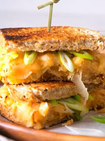Kimchi grilled cheese sandwiches stacked on serving tray with skewer.