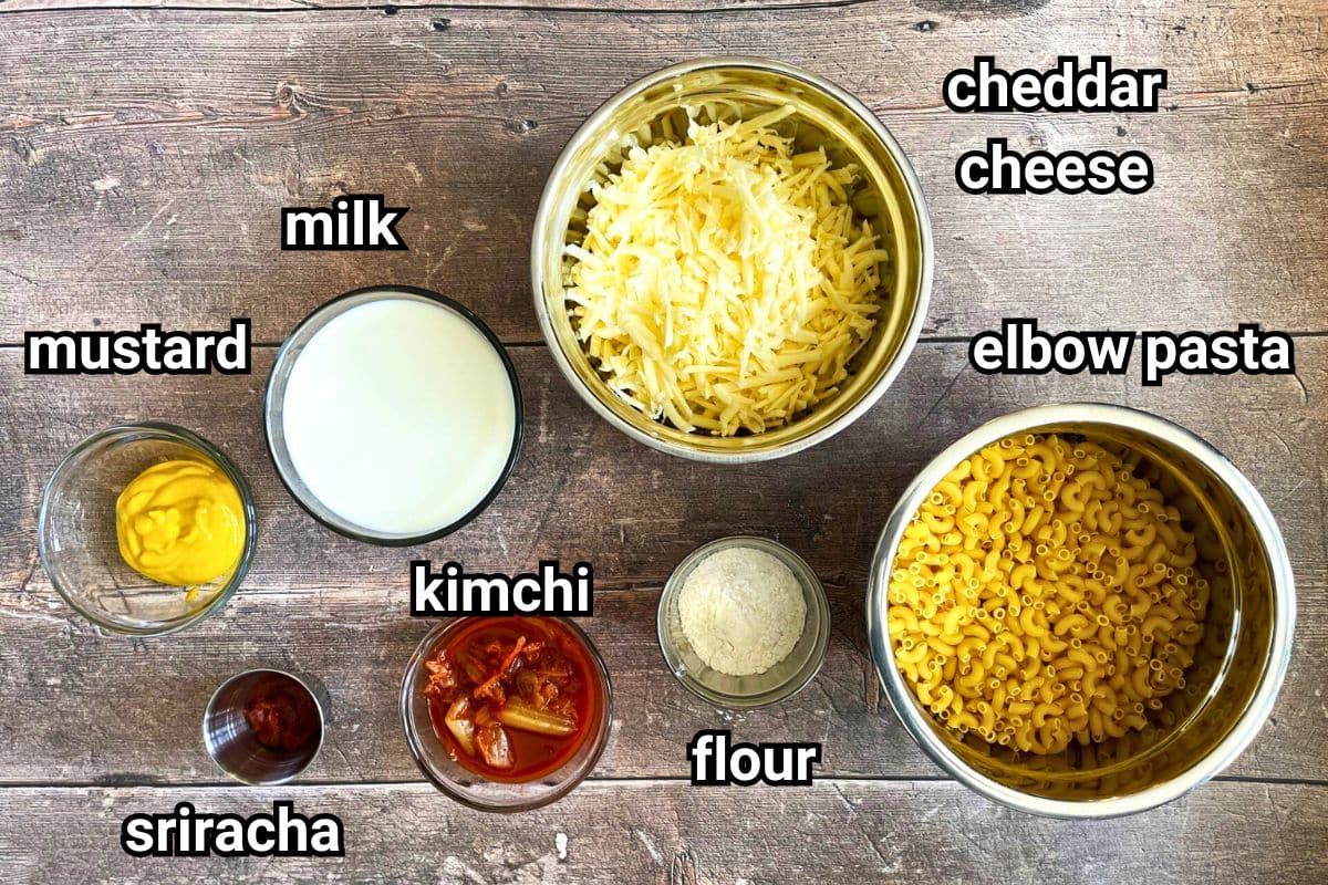 Kimchi mac and cheese ingredients prepped and labeled on wooden background.