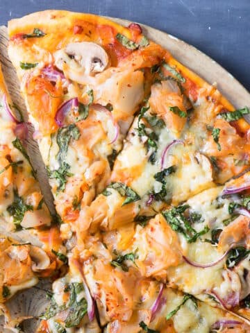Sliced kimchi pizza on round serving board.