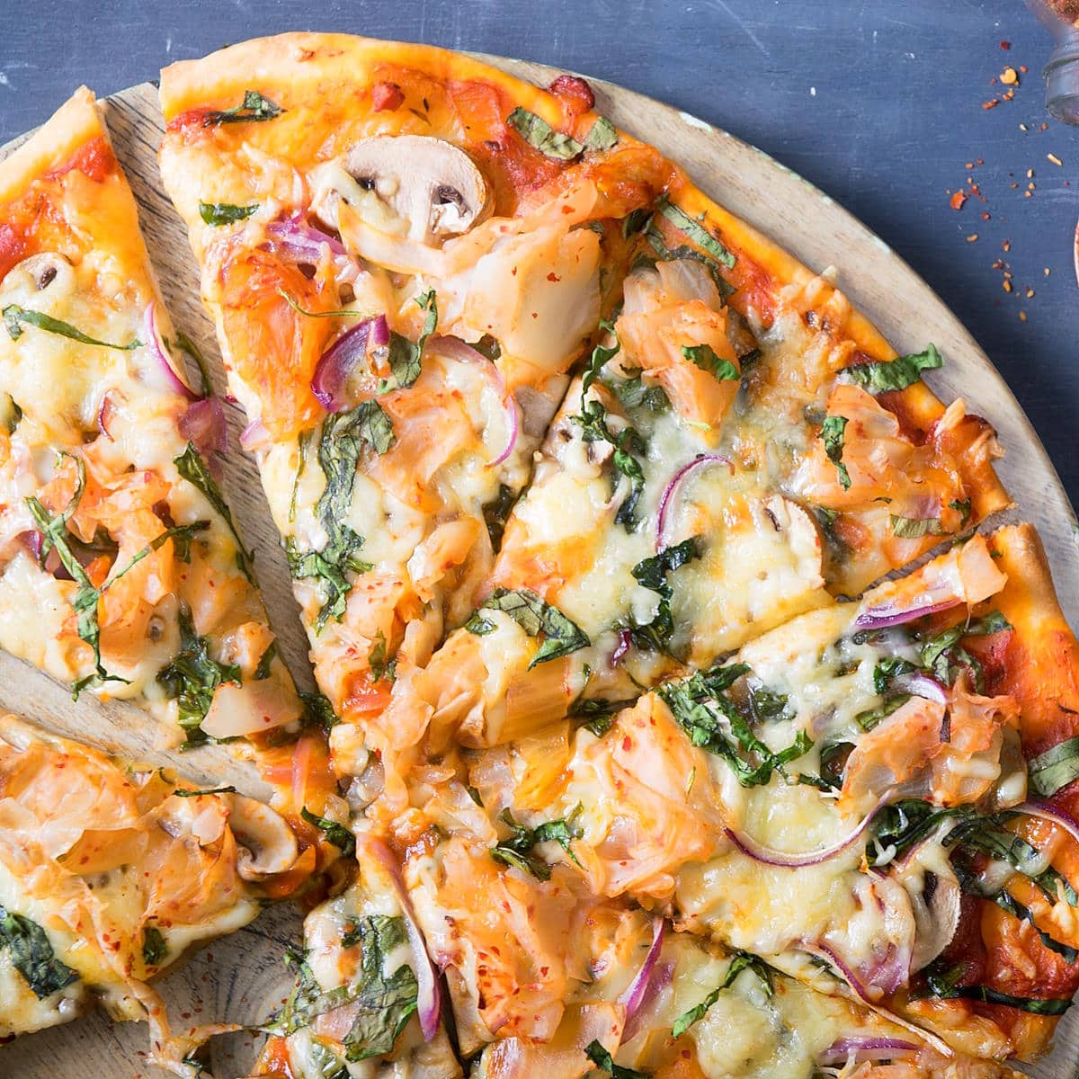 Sliced kimchi pizza on round serving board.