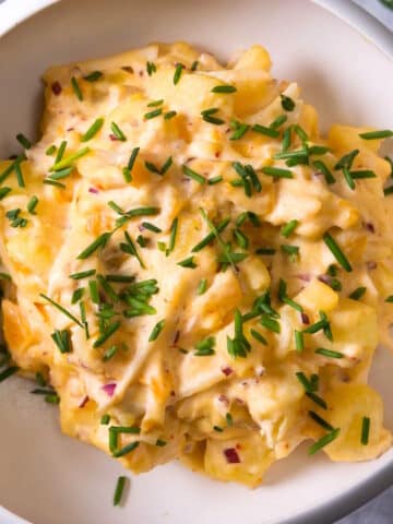 Kimchi potato salad with chives in white bowl.