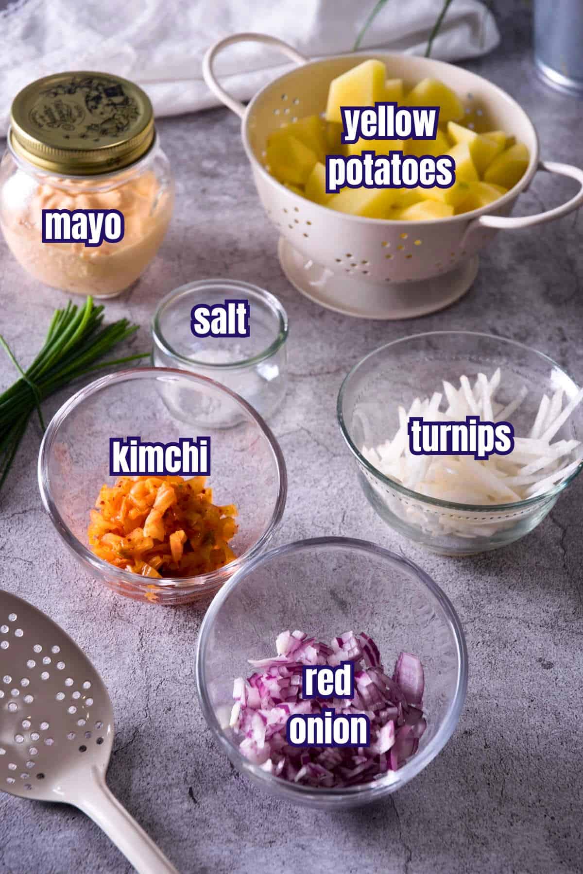 Kimchi potato salad ingredients prepped and labeled on grey background.