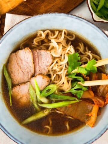 Kimchi ramen noodle soup in bowl with wooden chopsticks.