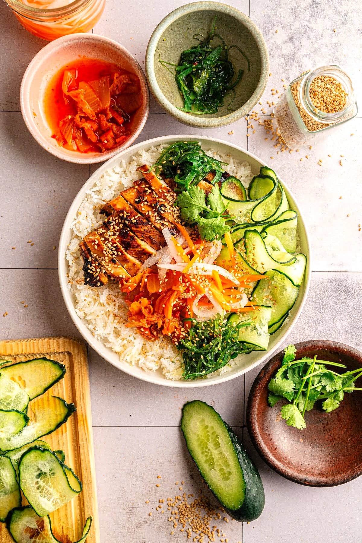 Kimchi rice bowl with kimchi, vegetables and sesame seeds on the side.