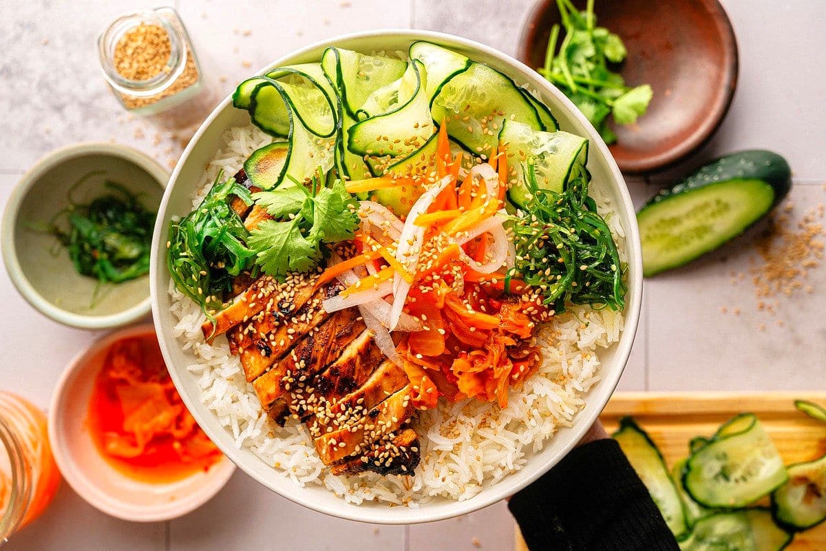 Kimchi chicken rice bowl with veggies in white bowl.