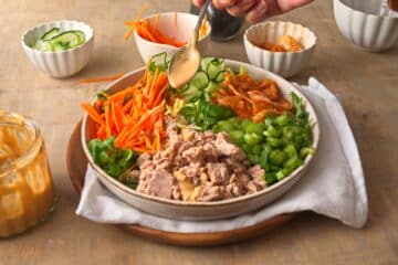 Kimchi salad with dressing getting drizzled over top.