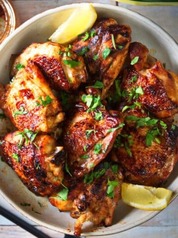 Korean kimchi chicken thighs in bowl with lemon wedges.