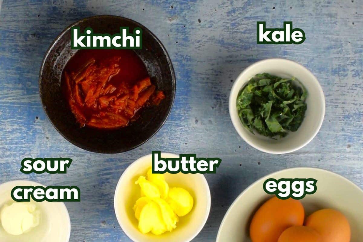 Kimchi scrambled eggs ingredients prepped and labeled on blue background.