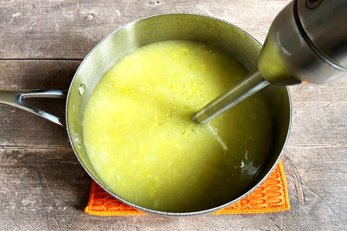 Potato leek soup getting blended with immersion blender in pot.