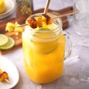 Mango ginger cocktail in glass with mango skewer, lime slice and straw.