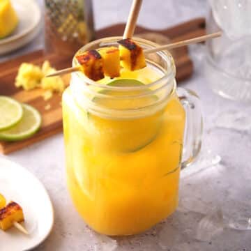 Mango ginger cocktail in glass with mango skewer, lime slice and straw.