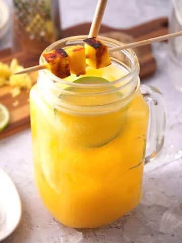 Mango ginger cocktail in glass with mango skewer, lime slice and straw.