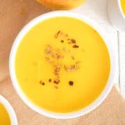 Mango soup in white bowl with spices on top.