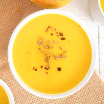 Mango soup in white bowl with spices on top.