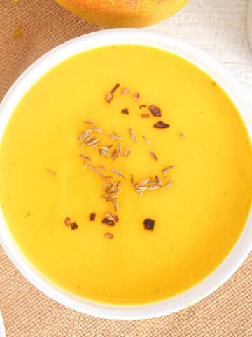 Mango soup in white bowl with spices on top.