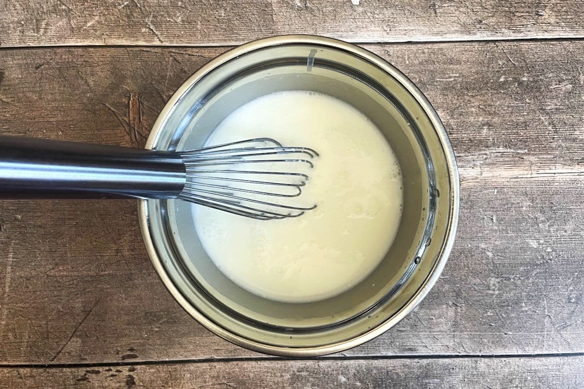 Yogurt and water in bowl with whisk.