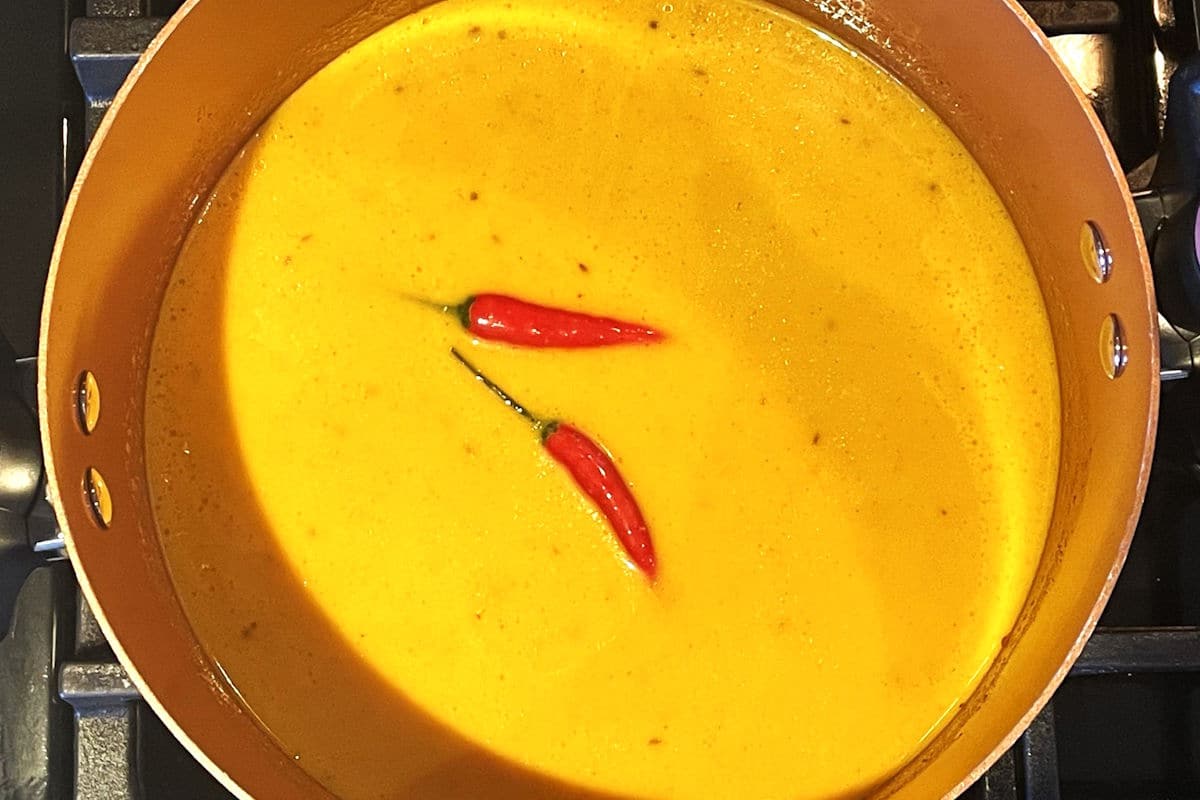 Mango soup in pot with chili peppers.