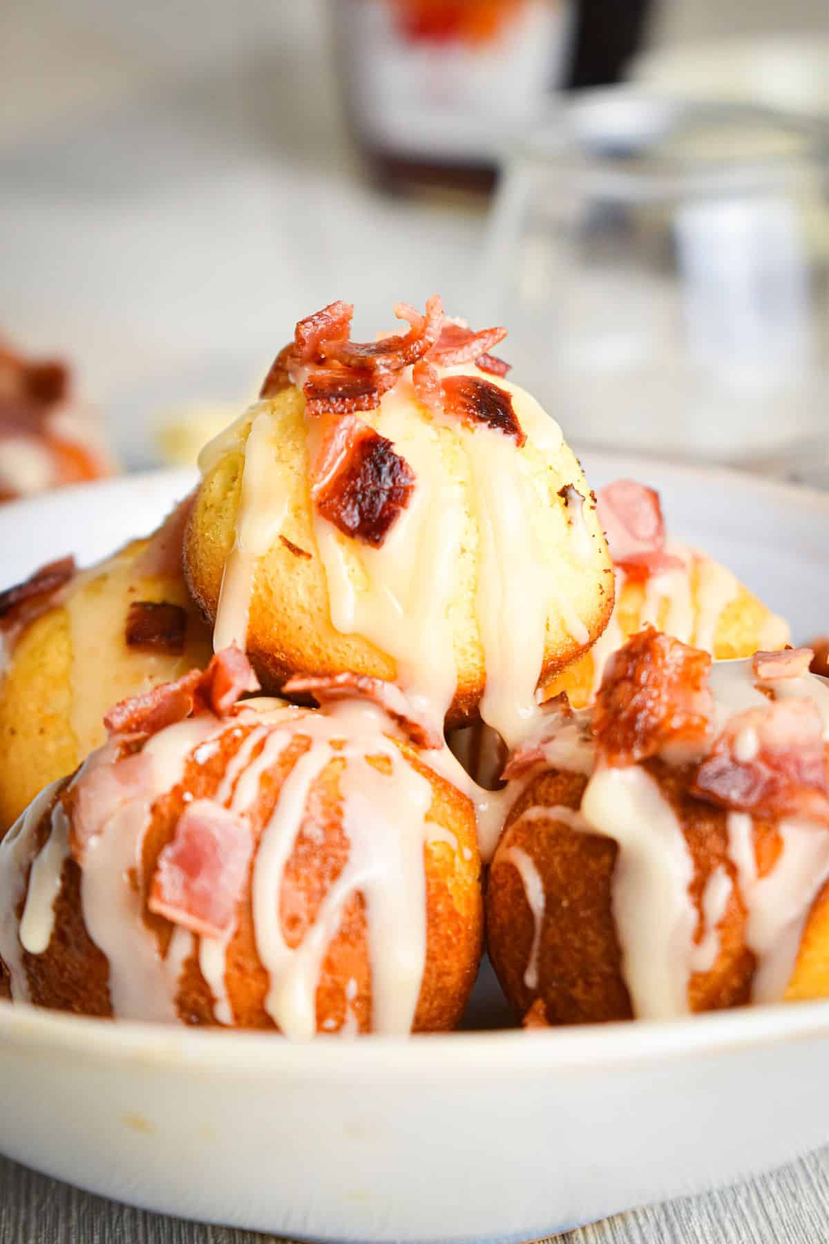 Maple bacon cake balls in bowl covered in maple frosting and glazed bacon bits.
