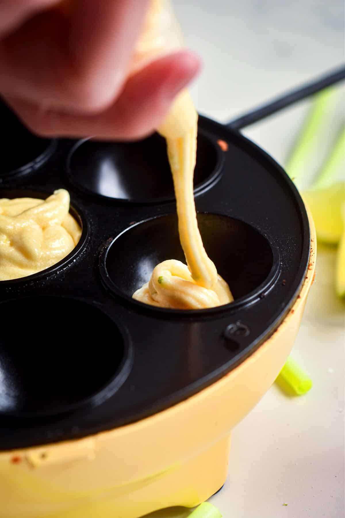 Margarita cake pop batter squeezing out of pastry bag into cake pop maker holes.