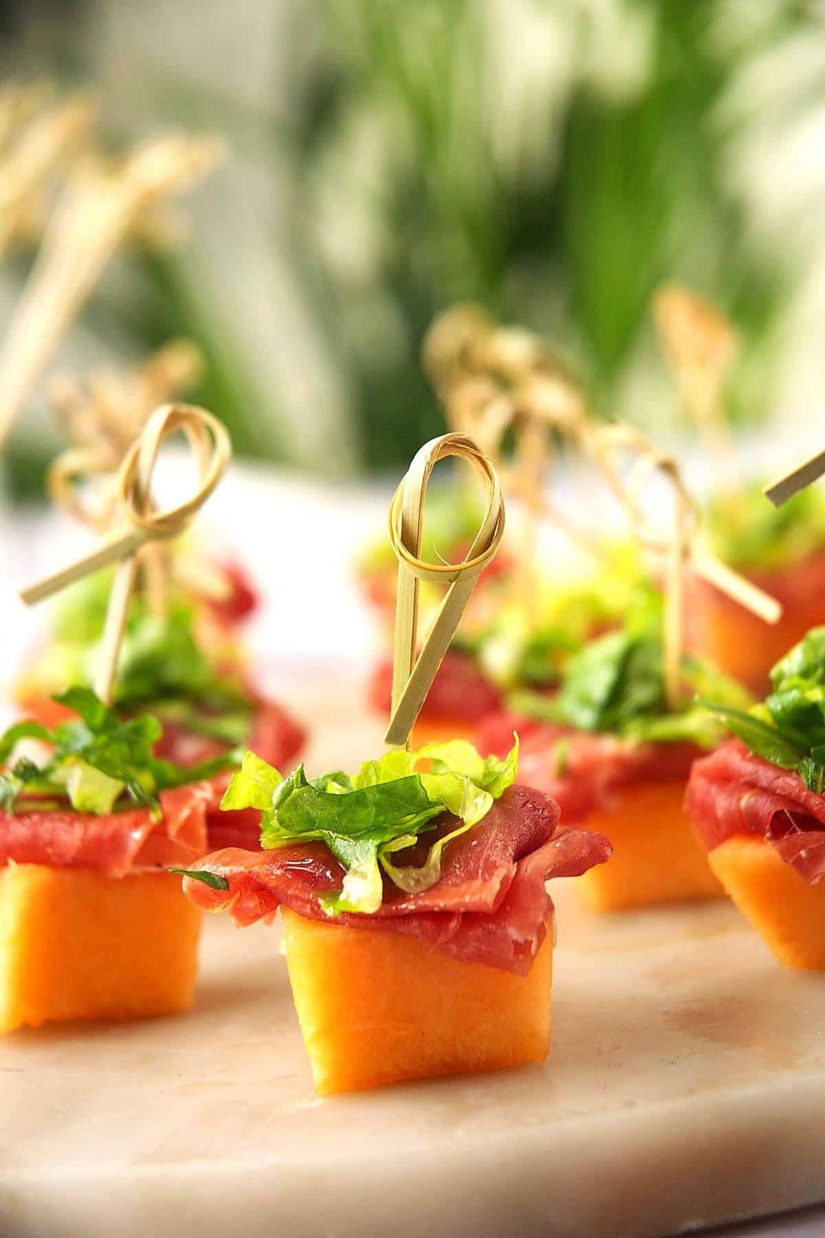Skewered melon and prosciutto appetizer on serving board.