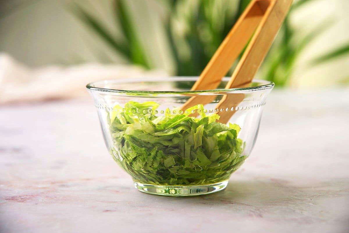 Diced greens in bowl with olive oil and small tongs.