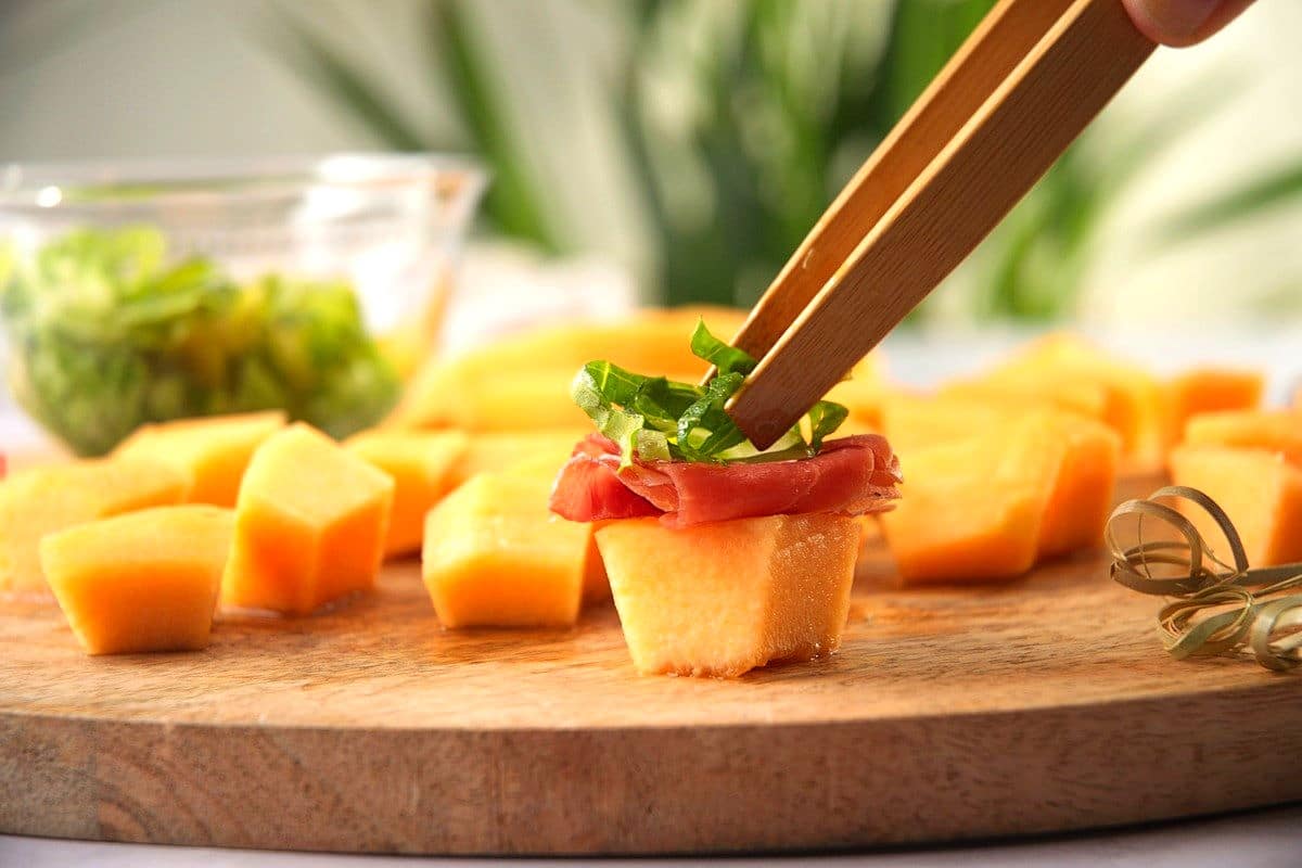 Melon cube with prosciutto slice and shredded greens.